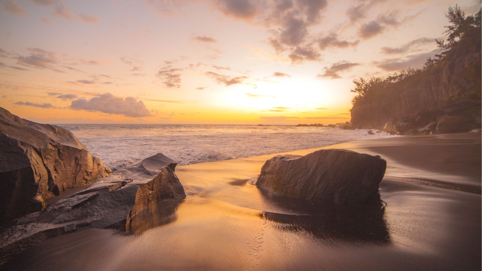 Plage de sable noir au coucher du soleil dans le Sud sauvage de La Réunion, avec rochers volcaniques et falaise