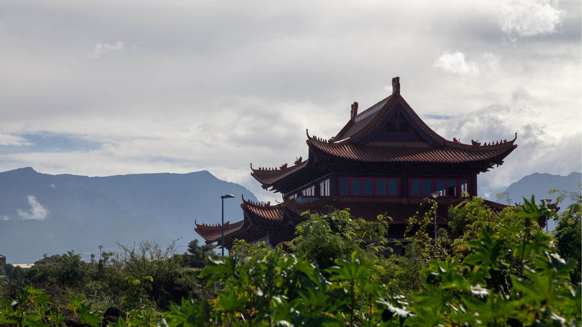 Temple chinois de Saint-Pierre entouré de végétation avec les montagnes de La Réunion en arrière-plan