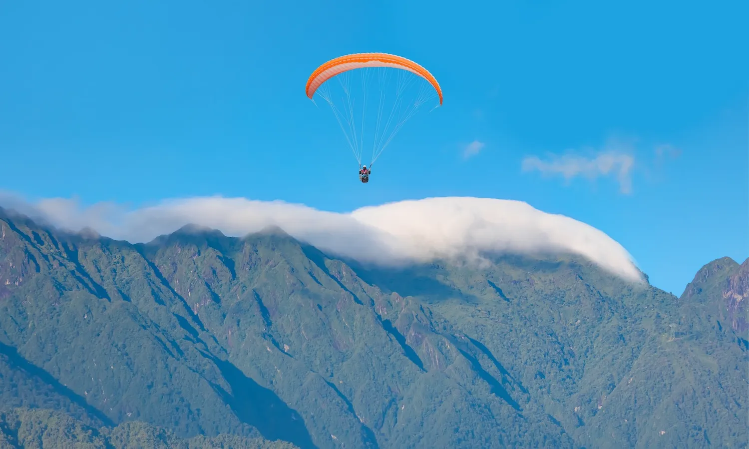 Vol en parapente avec voile orange au-dessus des montagnes verdoyantes de La Réunion